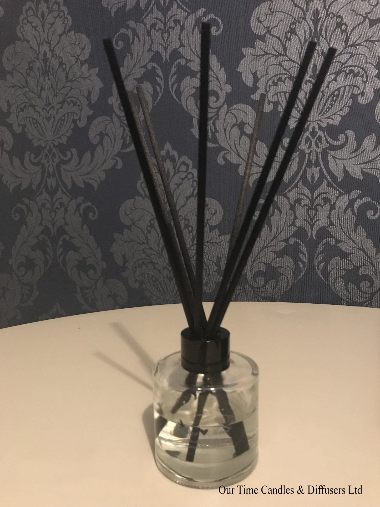 reed diffuser 100ml supplied in a clear bottle with black lid sat on a cream table