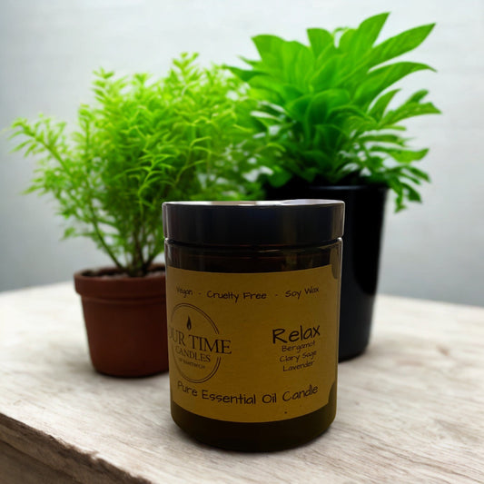 Jar of 'Relax' candle with plants in the background on a wooden surface