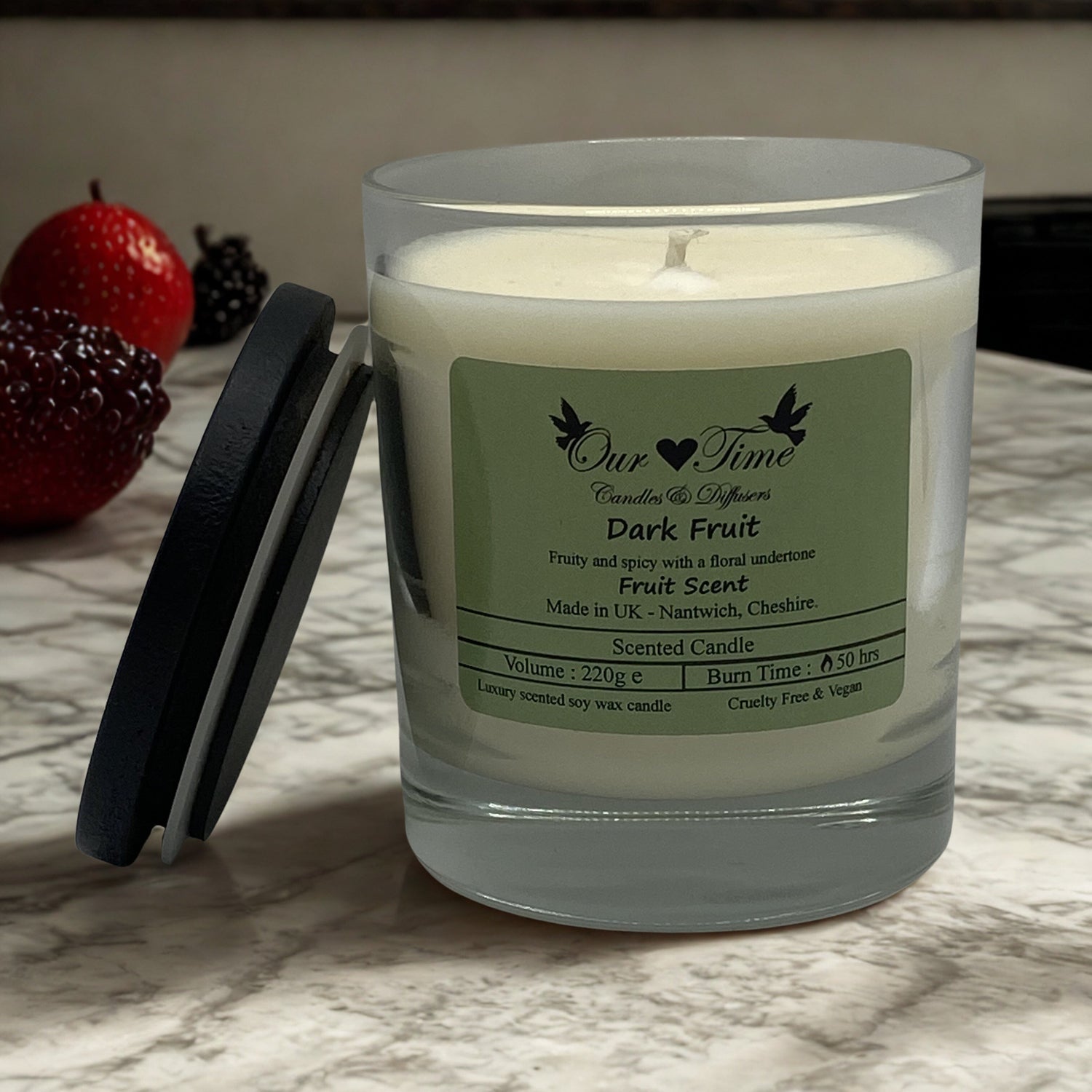 Large candle with black lid on a marble top with dark fruit in the background.