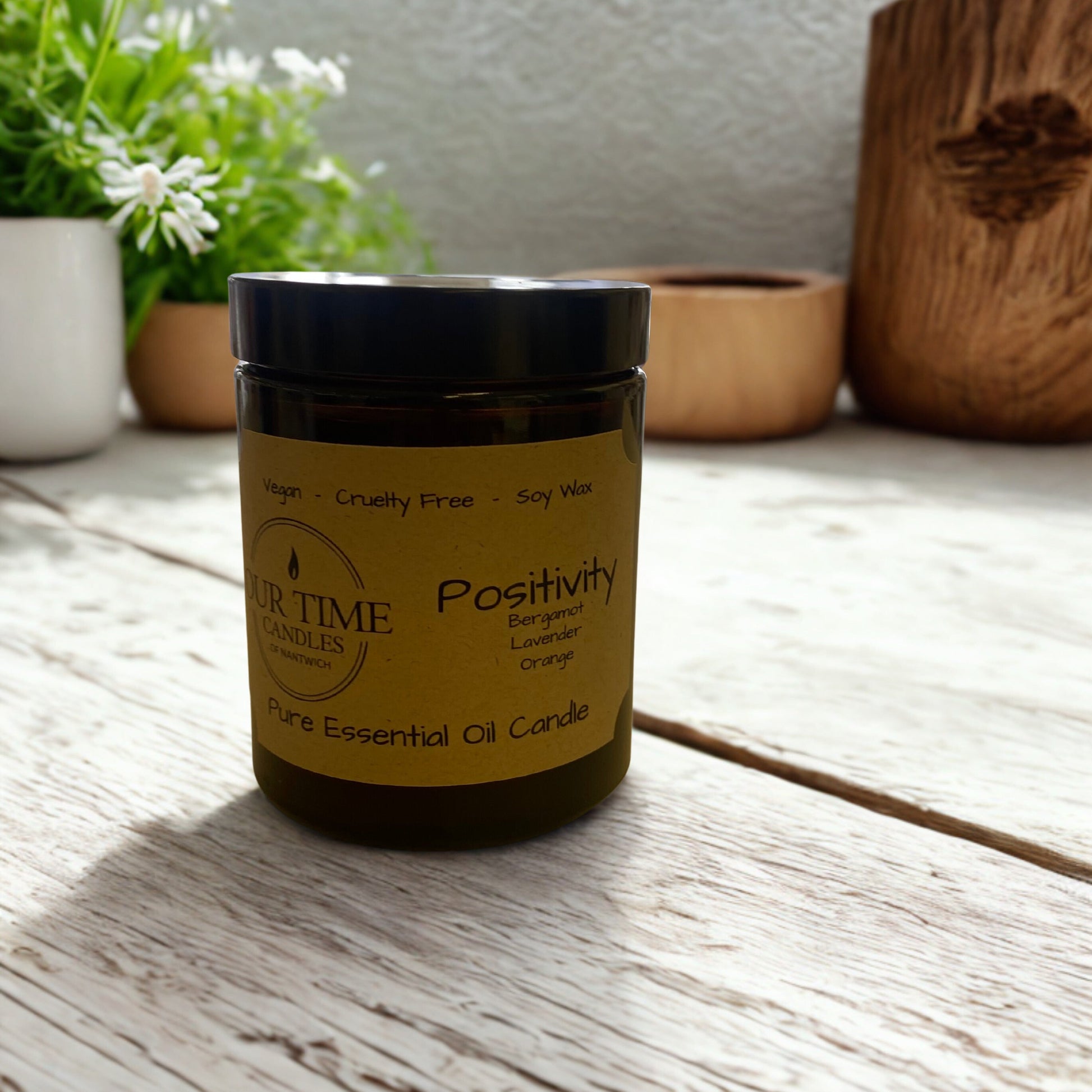 Candle labeled 'Positivity' on a wooden surface with plants in the background